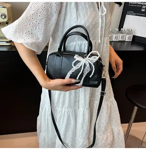 Détail du sac à main en cuir noir avec nœud en dentelle blanche et pendentif en perles