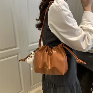 Bolso saco de cuero plisado color caramelo con cordón y pompón de piel blanca