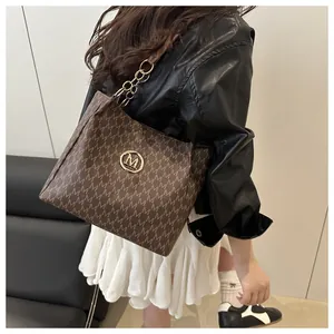 Vue détaillée du sac cabas marron avec motif M, chaîne dorée et logo métallique