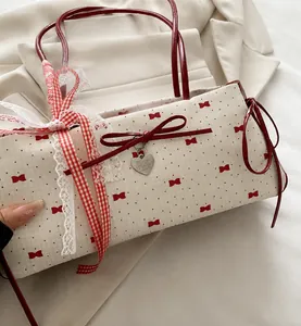 Close-up of beige shoulder bag featuring red bow prints and a silver heart pendant detail