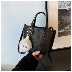Detail of black bucket bag featuring embossed patterns and a cute plush ball charm