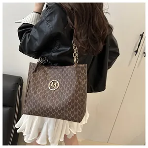 Gros plan sur un sac cabas marron avec motif de lettres et bandoulière dorée