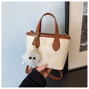 Detailed macro view of cream PU leather tote bag with embossed floral patterns and plush charm