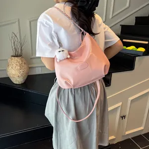 Sac hobo en cuir verni rose avec bandoulière chaîne et pompon porté à l'épaule