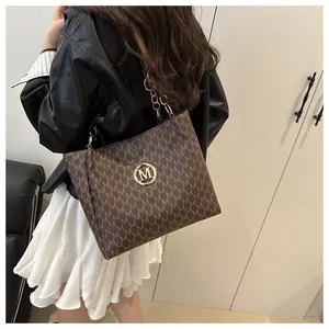 Détail d'un sac cabas marron foncé avec imprimé M et logo en métal sur modèle