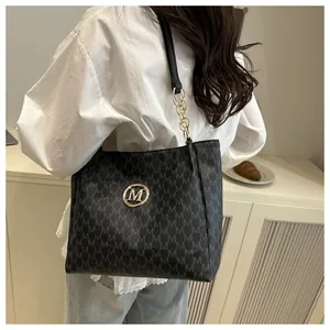 Sac fourre-tout noir avec imprimé lettres M et logo doré porté par un modèle