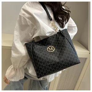 Détail d'un grand sac cabas noir avec motif M gris et logo en métal doré sur un modèle