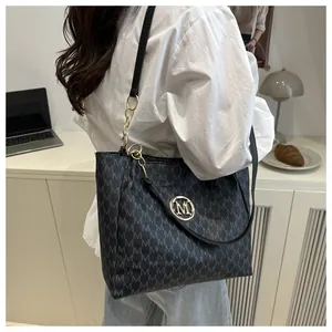 Détail d'un sac cabas noir avec motif M et bandoulière en chaîne dorée porté par un mannequin