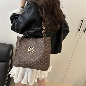 Sac croissant marron avec imprimé monogramme M et logo doré porté par modèle