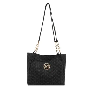 Sac cabas noir avec motif M embossé et bandoulière chaîne dorée sur fond blanc