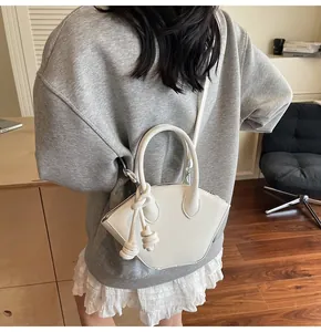 Détail d'un sac à main blanc géométrique avec breloques à nœuds porté par un mannequin