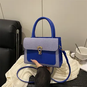 Royal blue crossbody bag with leather texture and gold buckle on a white tablecloth