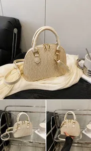 Detalle del bolso de paja beige en forma de concha con cremalleras doradas y mango