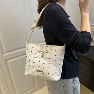 Borsa a tracolla bianca con ricami a fiocco e ciondolo a cuore su una modella