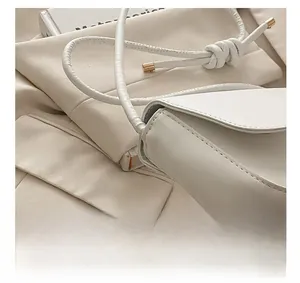 Detail of white leather shoulder bag featuring gold metal tips and fine stitching accents