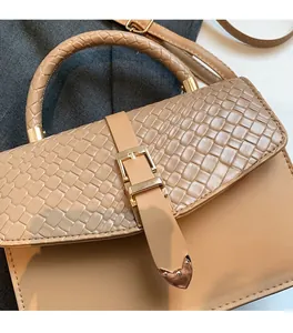 Close-up of beige crossbody bag showing woven flap texture and gold metal heart buckle detail