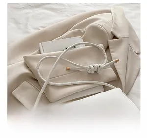 Detail of white minimalist handbag with slim leather knotted strap and gold hardware