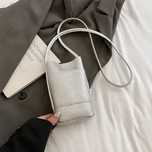 Détail du mini sac bandoulière argenté avec texture litchi sur un fond de blazer élégant