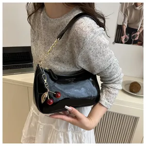Close-up of black patent leather shoulder bag with cherry charm and metal chain detail