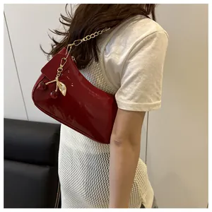 Detail of red patent leather shoulder bag with cherry pendant and gold chain strap