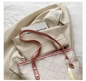 Detail showing jacquard texture, pink leather handles, and white fringe tassel on a tote bag