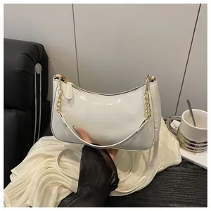 Detail of white patent leather crescent bag with gold chain and printed fashion logo