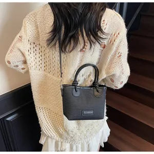 Detail of black mini bucket bag with textured weave and Fashion label on beige knit