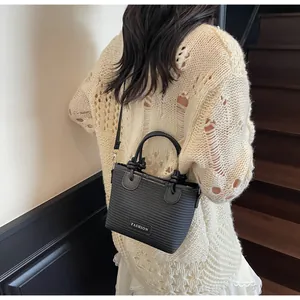 Detail of black bucket bag with fashion label and knot handles on a casual model