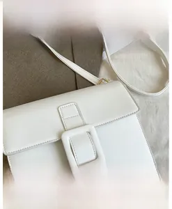 Detail view of a white leather square crossbody bag with decorative buckle and neat stitching