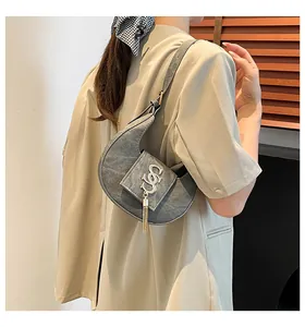 Dettaglio borsa a mezzaluna grigia con logo dorato e nappa su blazer beige