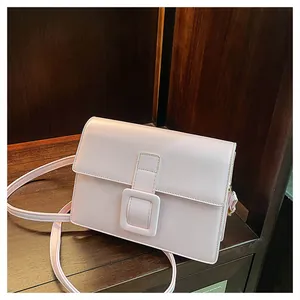 Detail view of a pale pink crossbody bag with a large square buckle on dark wood shelves
