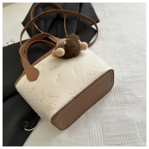 Top view of beige and brown bucket bag with embossed playful patterns and plush charm