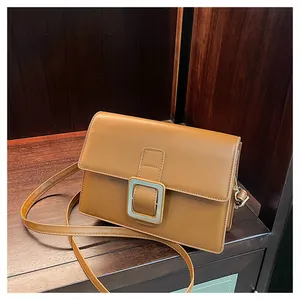 Detail shot of brown leather crossbody bag with square silver buckle on wooden shelf