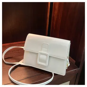 Detail view of a white leather square crossbody bag with large buckle on wooden shelf