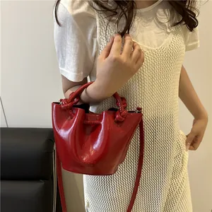 Glossy red bucket bag with woven handle and crossbody strap shown on a model