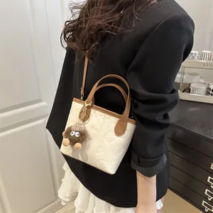 Cream white bucket bag with embossed patterns, brown straps and a cute plush charm