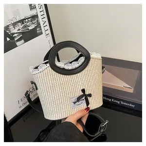 Detail shot of woven straw bag with white lace trim, black leather handles, and bow charm