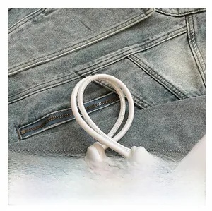 Détail de la bandoulière en cuir blanc rembourré avec nœud sur fond en denim