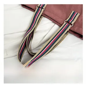 Detail of colorful striped fabric shoulder strap on a burgundy tote bag with logo