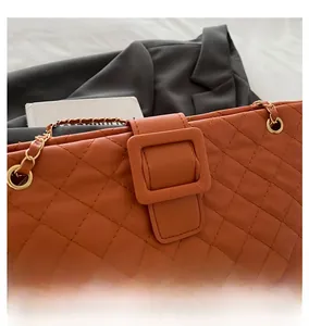 Detail of orange quilted leather shoulder bag featuring metal chain and square buckle