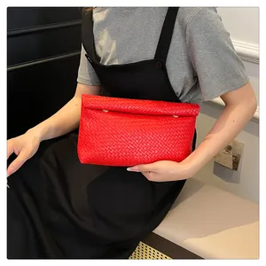 Close-up of red woven leather envelope clutch bag held by model in a minimal setting