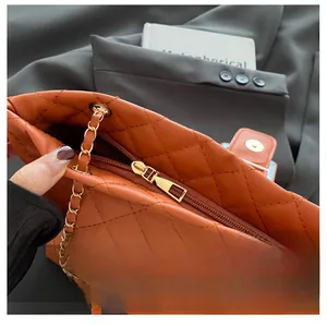 Detail of smooth gold zipper and orange quilted leather texture on crossbody tote