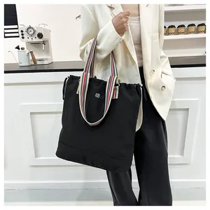 Detail of black canvas tote bag with colorful striped handles and silver clover logo