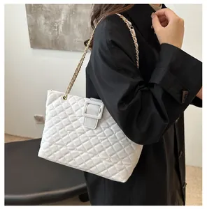 Detail of white quilted tote bag featuring a large square buckle and gold chain strap