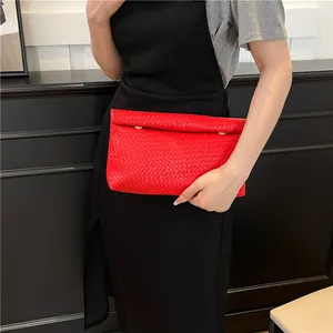 Fashionable red woven envelope clutch bag with gold buckles held by a model in black dress