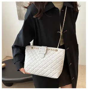 Close-up of white quilted tote bag with golden chain strap on model in black coat