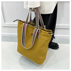 Close-up of ginger yellow canvas tote bag featuring striped handles and drawstring closure