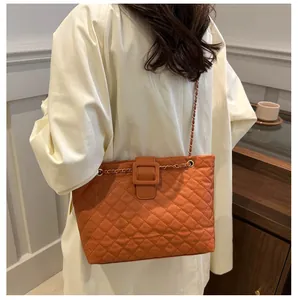 Lifestyle view of orange quilted tote bag with chain strap worn by a female model