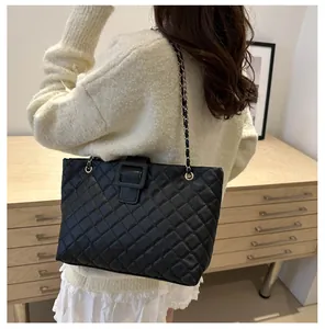 Detail of black quilted tote bag with chain strap shown on a model in home setting