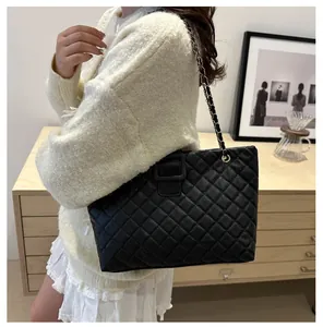 Detail of a black quilted tote bag with chain strap worn by a model in a casual setting